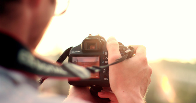 Bilden föreställer en DSLR, digitalkamera som hålls upp mot solnedgången
