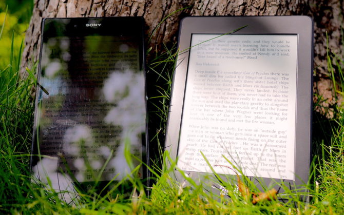 En Sony Z Ultra tablet och en Amazon Kindle Paperwhite står mot ett träd i solljus. Det går knappt att se vad det står på Sonyn, men texten på Kindle är tydlig.